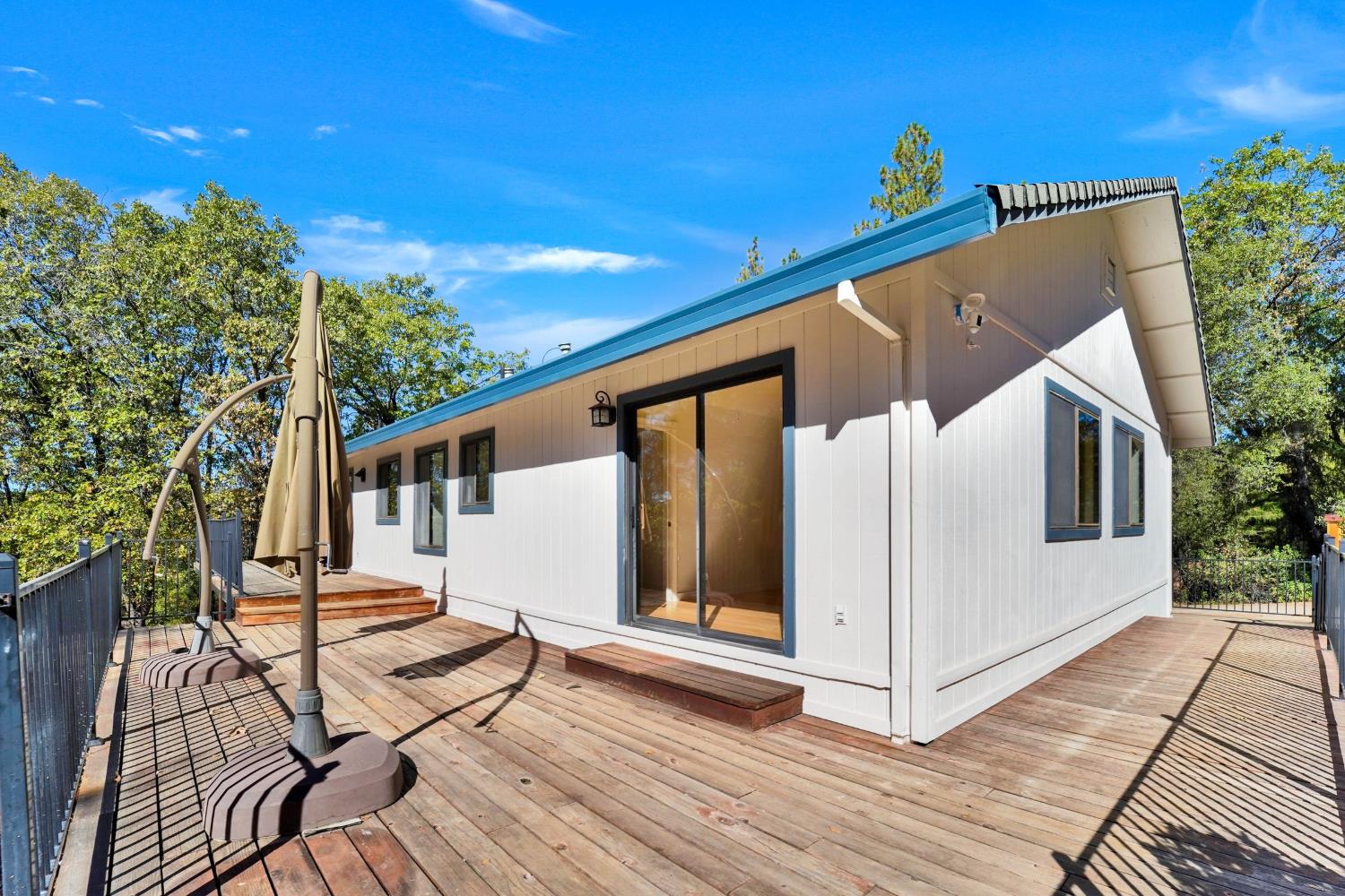 Single-story home with blue trim and sliding glass doors opening onto a spacious wood deck.