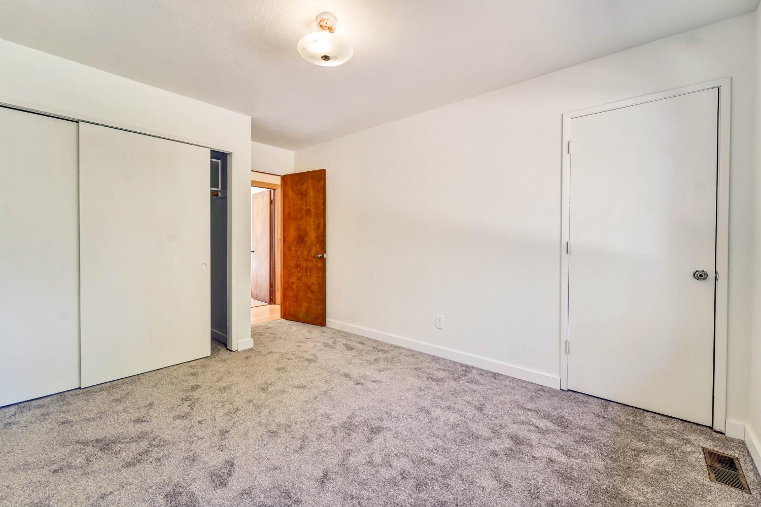 Empty carpeted room with a sliding closet door and open wooden doorway.