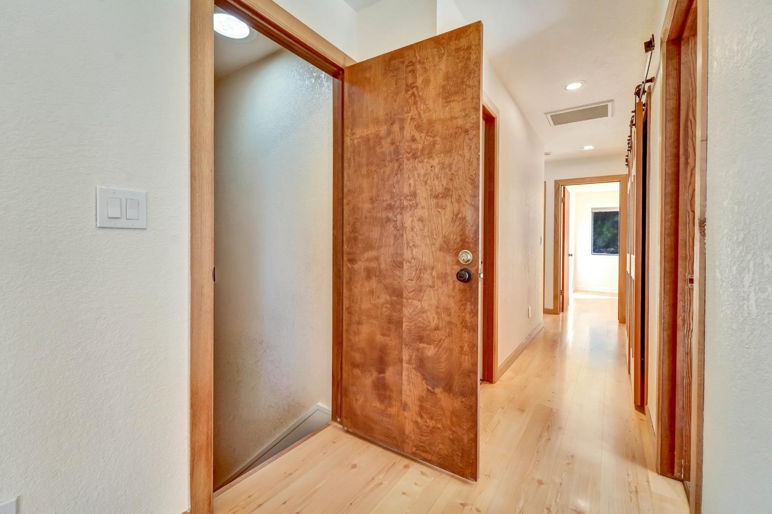 Hallway with light wood floors, warm wood trim, and an open door beside a stairwell.