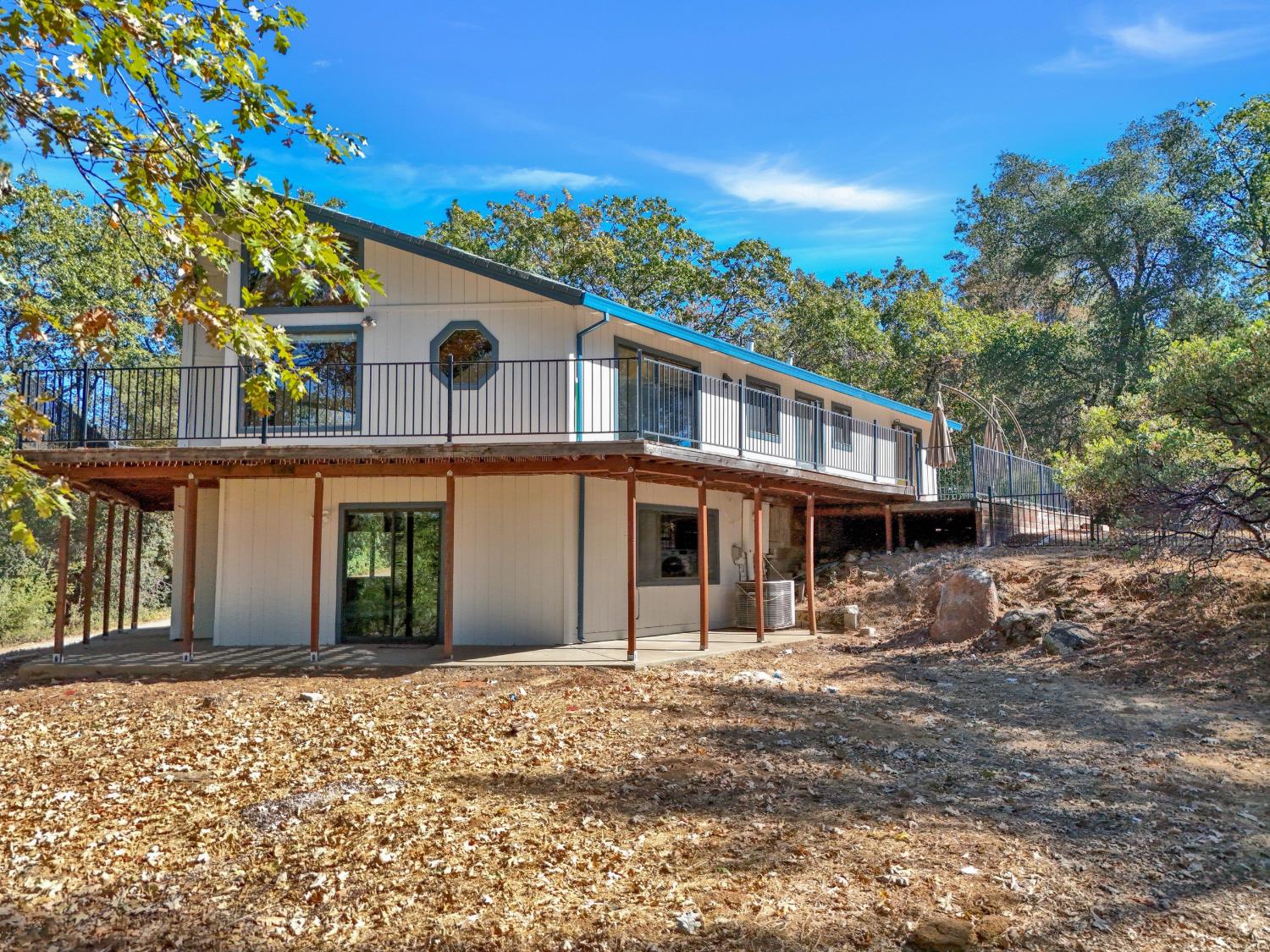 Two-story home on a wooded slope, with a long elevated deck and covered lower patio.