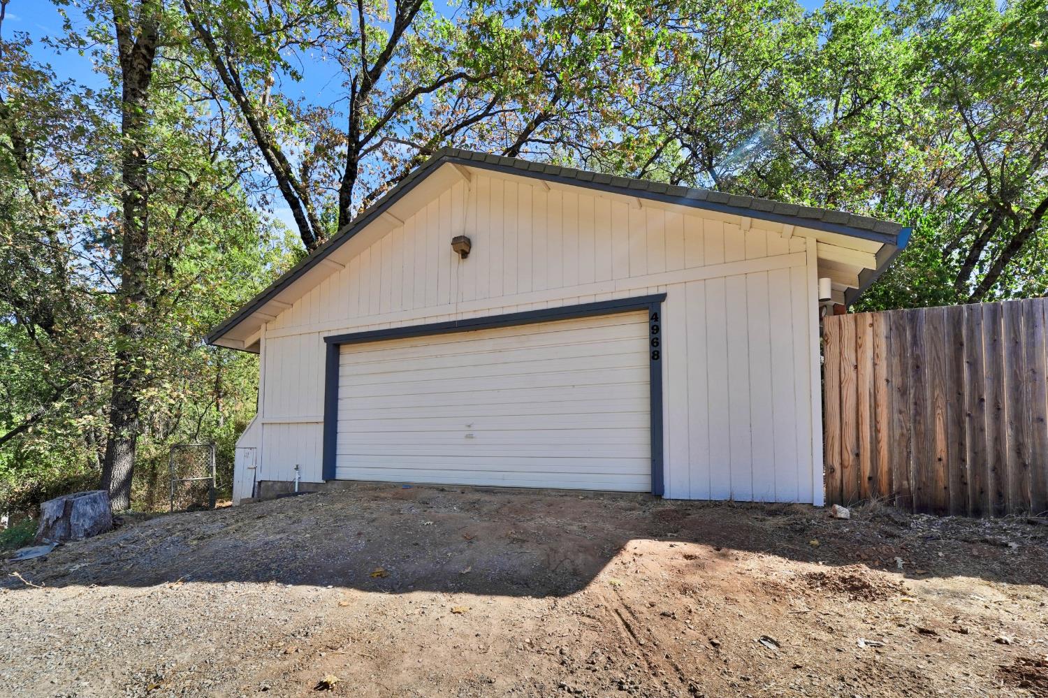 Detached garage with a white door and blue-gray trim, surrounded by trees and a wooden fence.