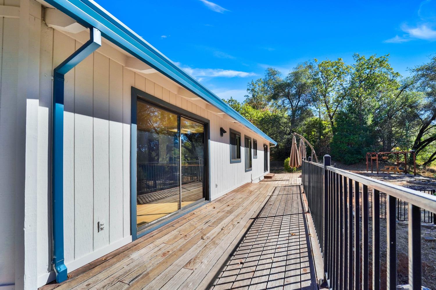 Wooden deck beside a sliding glass door, with black railing and trees beyond.