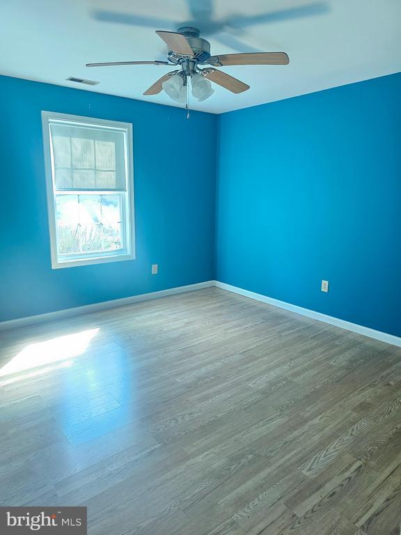 Empty blue room with gray wood-look flooring, a window, and a ceiling fan.