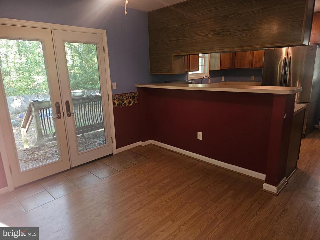 Kitchen with a red peninsula, dark wood cabinets, stainless refrigerator, and French doors to a wooded deck.