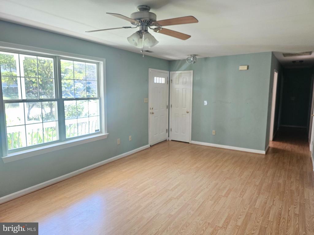 Vacant living room with pale blue-green walls, light wood floors, a large window, and ceiling fan.