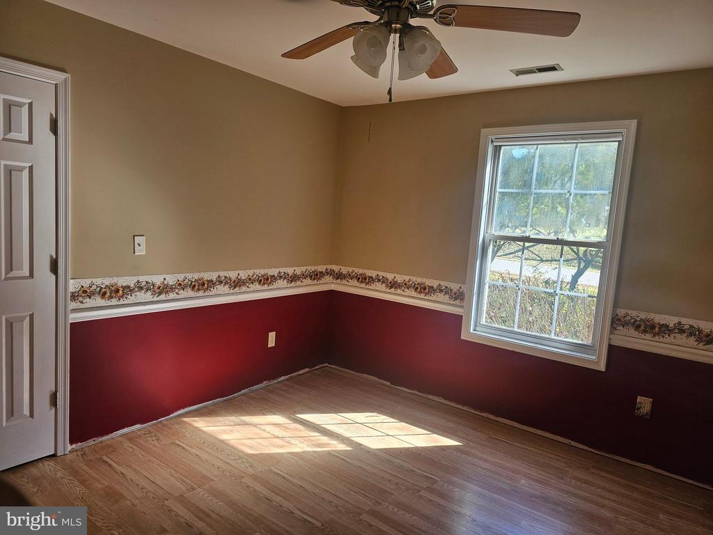 Empty room with wood-look flooring, burgundy lower walls, floral border, ceiling fan, and sunlit window.