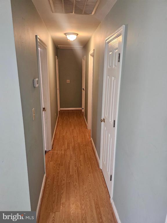 Hallway with wood-look flooring, several white doors, and a ceiling access panel.