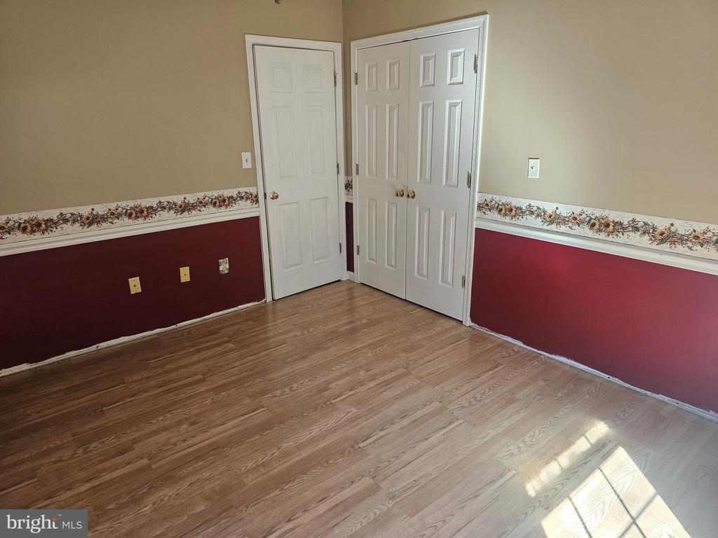 Empty room with burgundy and tan walls, floral border, wood-look flooring, and white closet doors.