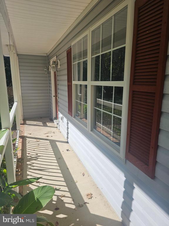 Covered porch with large windows, red shutters, and a sunlit concrete walkway.