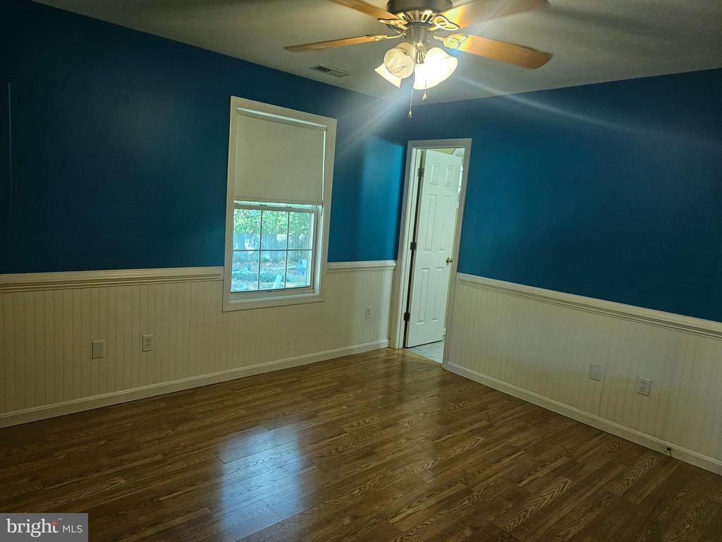 Empty room with teal walls, white wainscoting, hardwood floors, and a ceiling fan.