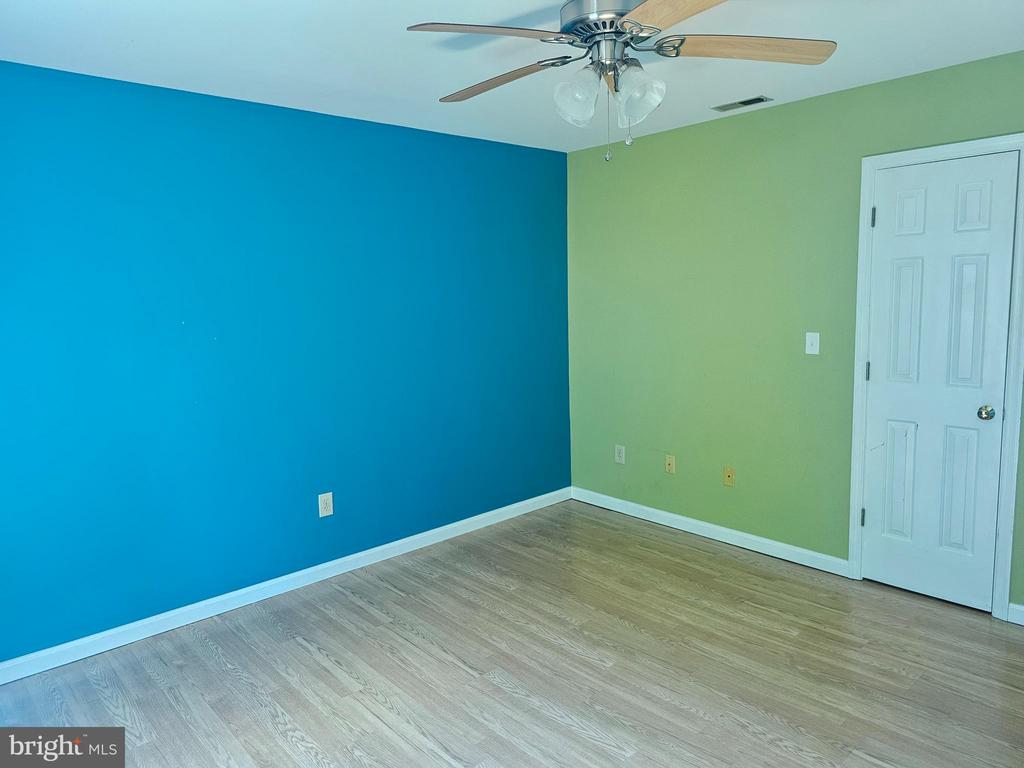 Empty room with blue and green walls, wood-look flooring, and a ceiling fan.