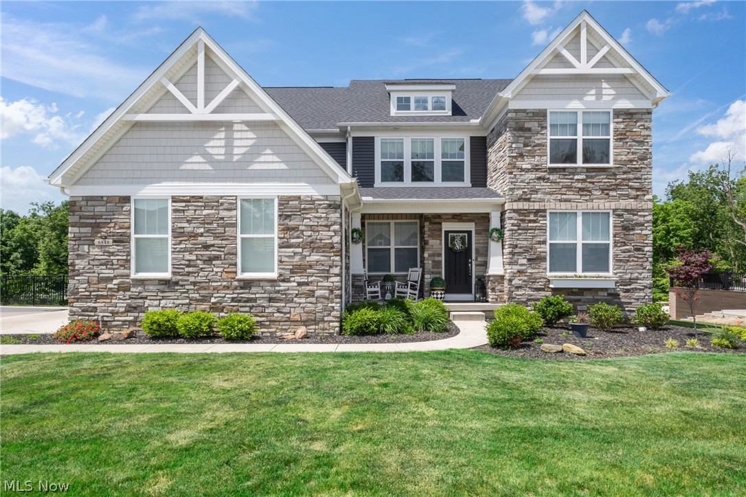 Two-story stone-and-siding home with white-trimmed gables, a covered porch, and a landscaped front lawn.