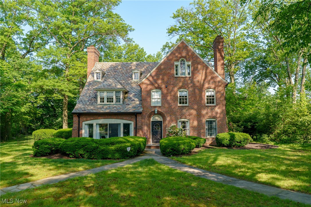 Two-story red brick house with a steep roof, mature trees, and a walkway to the front door.