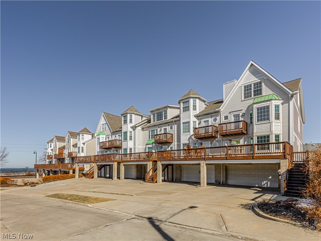 Attached white townhomes with raised decks, balconies, and garages; water is visible in the distance.