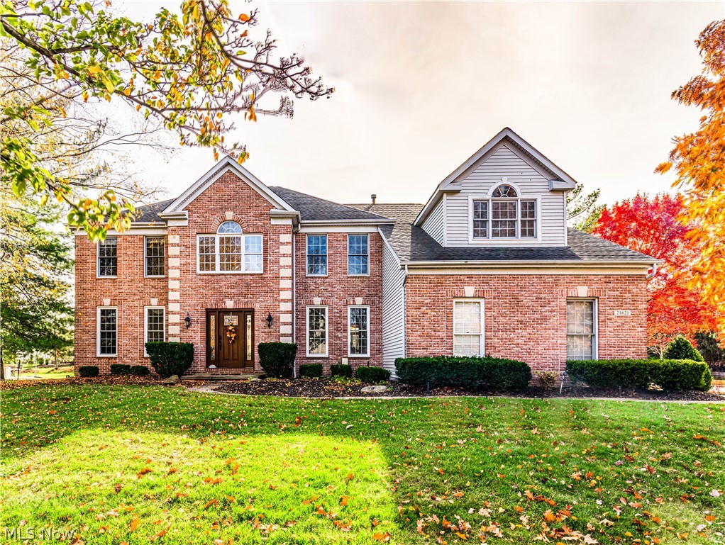 Two-story brick-and-siding house with a broad lawn and autumn trees.