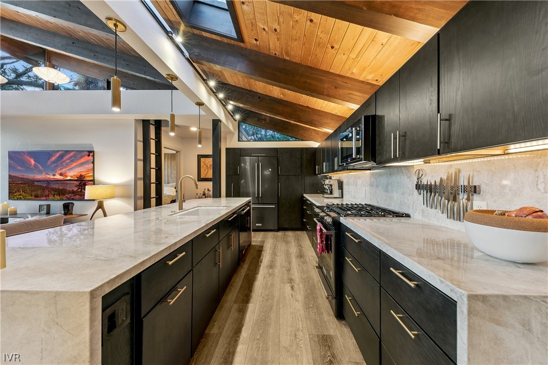 Modern kitchen with dark cabinets, stone counters, and a vaulted wood ceiling with skylights.