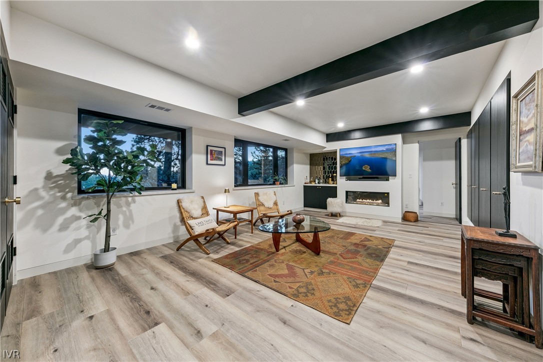 Living room with exposed ceiling beams, large windows, and a modern fireplace.