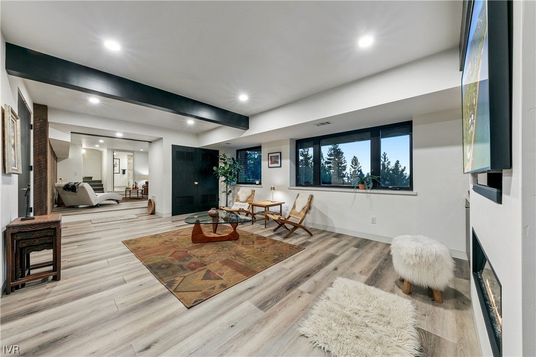 Furnished living room with large tree-facing windows, a dark ceiling beam, and a fireplace.