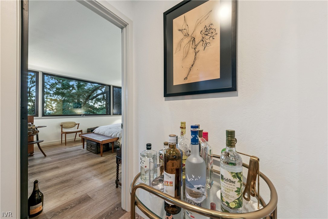 Bedroom with large windows and wood floors, viewed past a brass bar cart with liquor bottles.