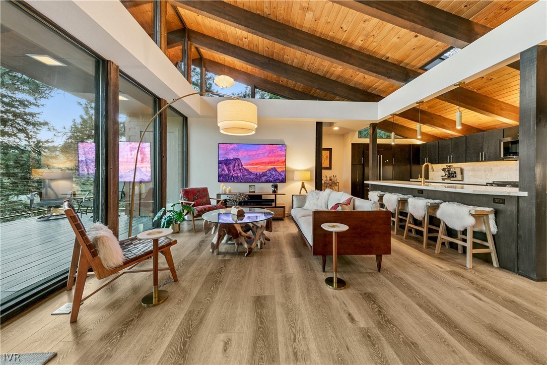 Open-plan living room and kitchen with vaulted wood ceiling and sliding doors to a wooded deck.