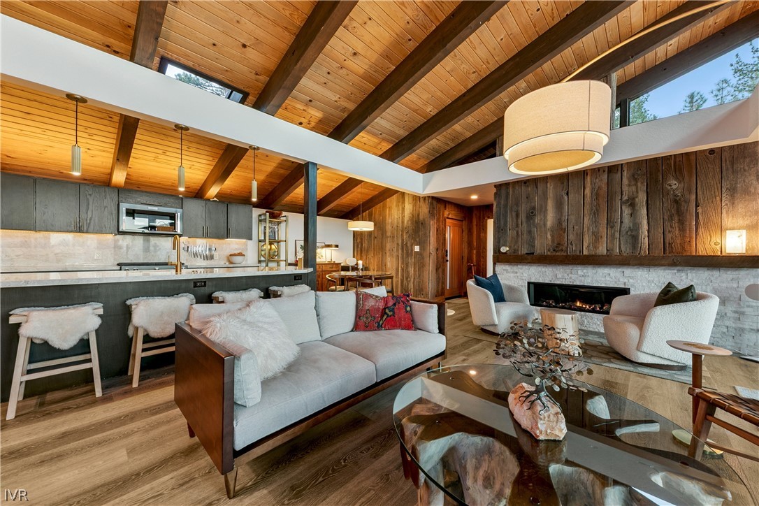 Open-plan living room with vaulted wood ceiling, exposed beams, and a stone fireplace.