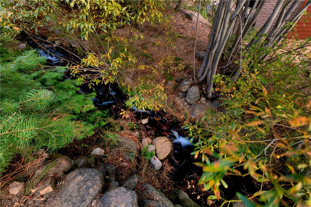 A small creek winds through rocks and autumn foliage beside a home.