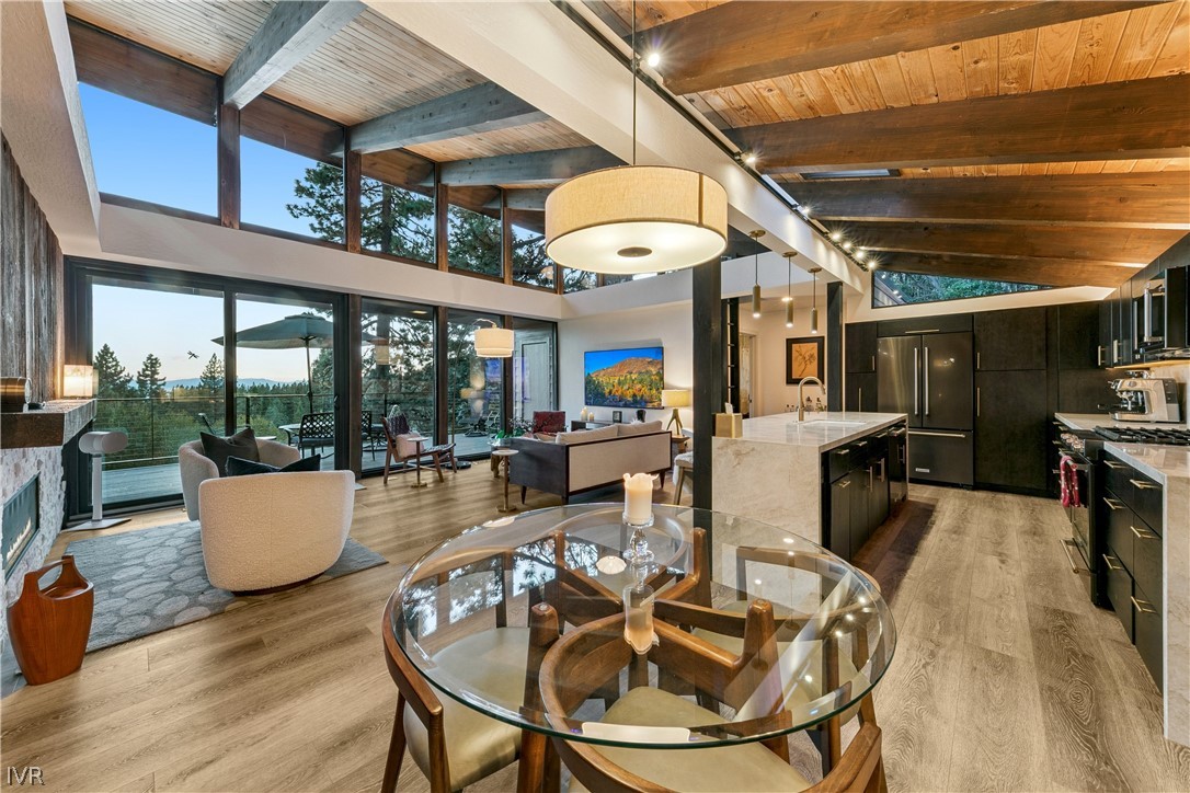 Open living room and kitchen with vaulted wood ceilings, tall windows, and a glass dining table.