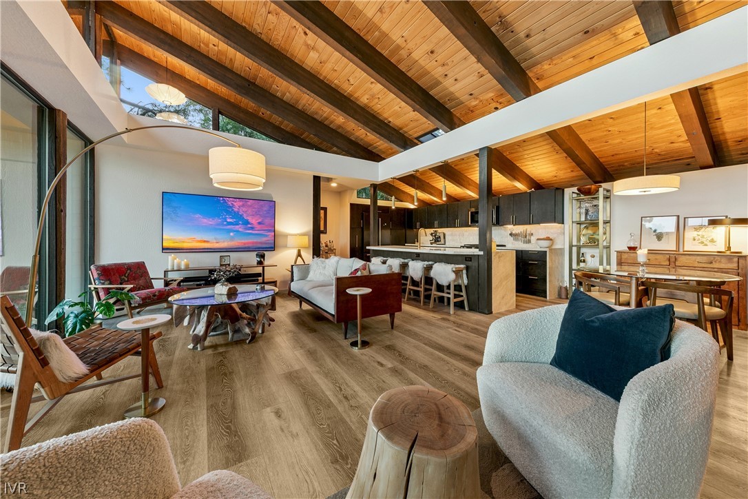 Open-plan living room with a vaulted wood ceiling, exposed beams, and adjoining kitchen and dining area.