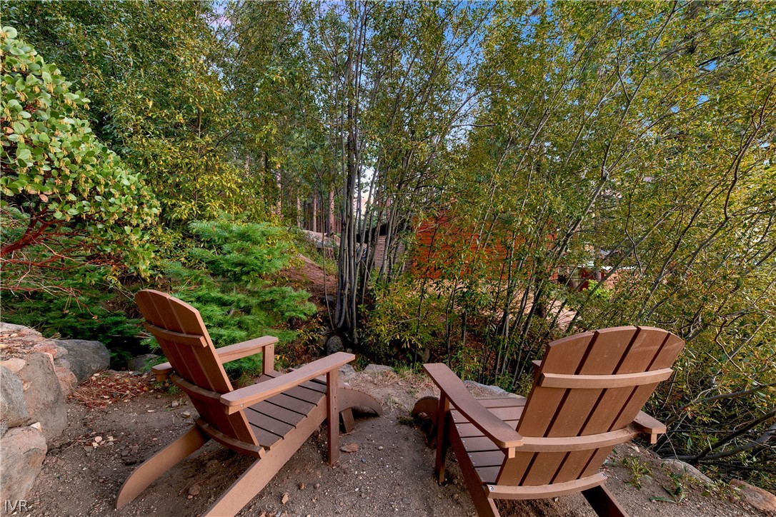 Two Adirondack chairs sit on a gravel terrace amid dense trees and autumn foliage.