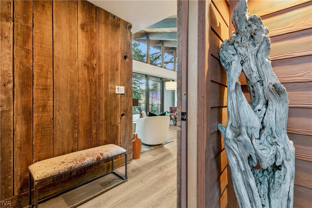 Home entry with a rustic plank wall, cushioned bench, and driftwood sculpture beside the open door.