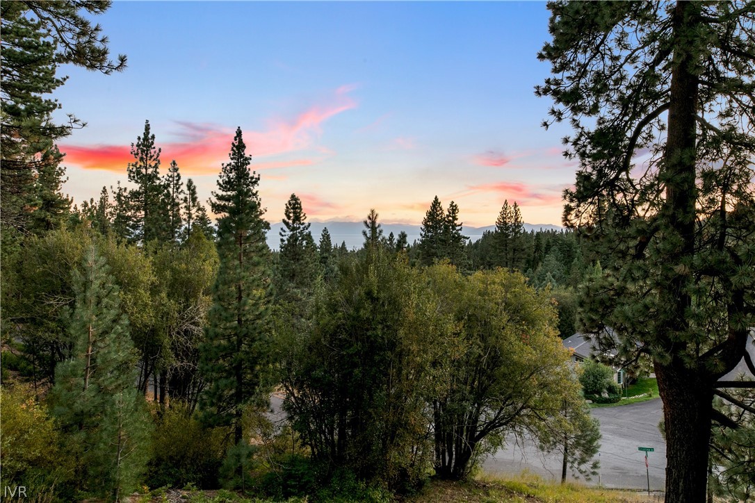 Wooded property view with a distant ridgeline and pink sunset clouds