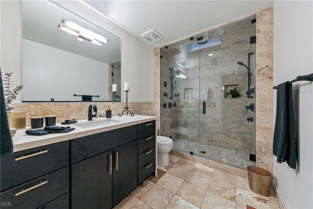 Bathroom with a dark wood vanity and a glass-enclosed beige stone shower.