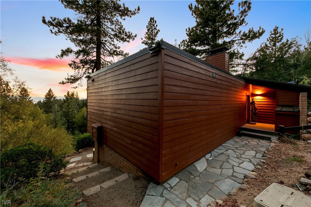Wood-sided home with a stone walkway leading to its warmly lit entrance at dusk.