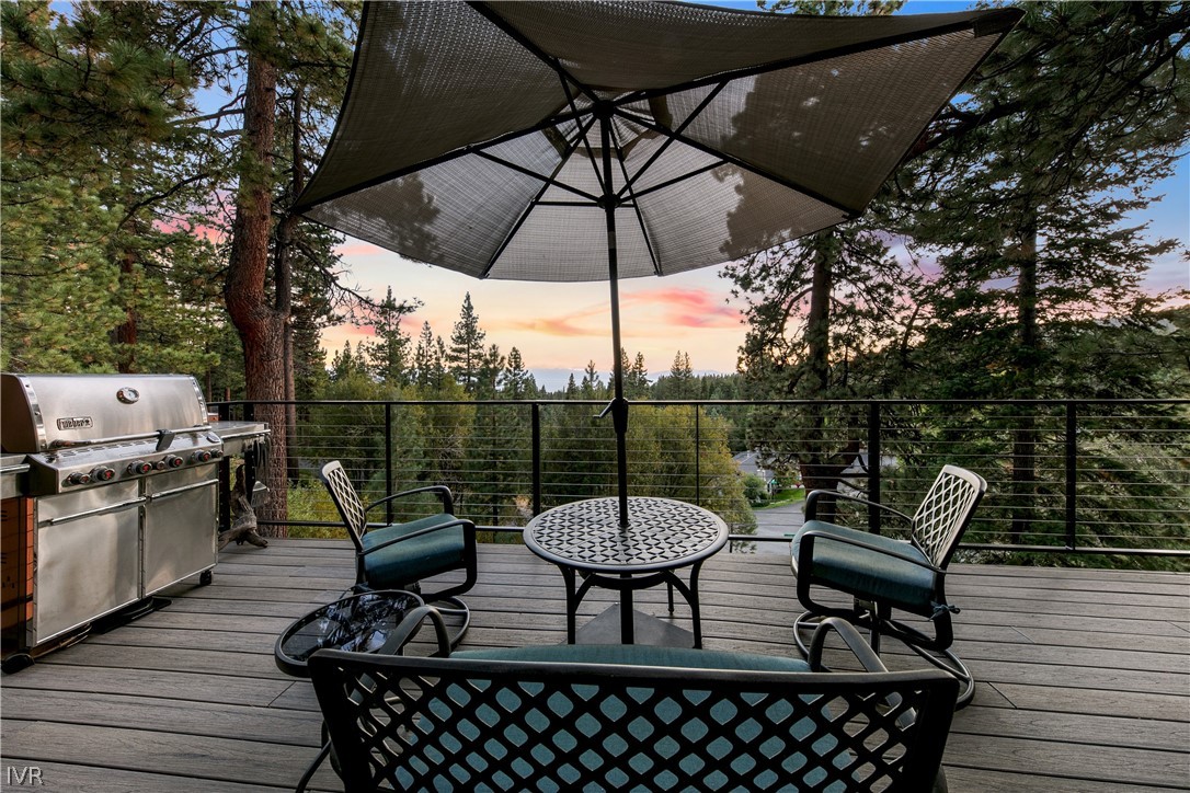 Furnished deck with grill, seating, and sunset views through pine trees.