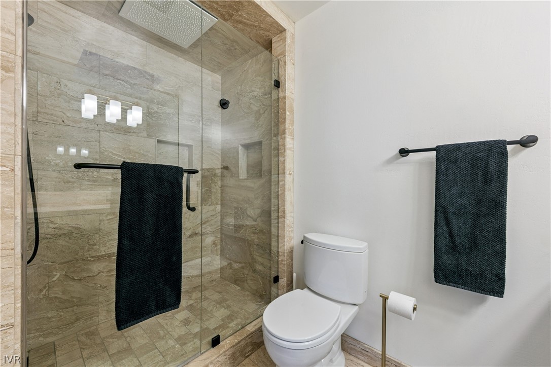 Bathroom with a marble-tiled glass shower, rain showerhead, toilet, and dark towels.