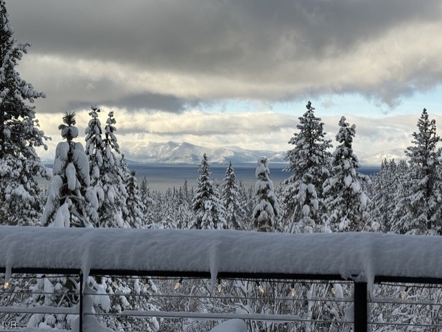 Snow-covered pines frame a lake and distant mountains beyond a snow-covered balcony railing.
