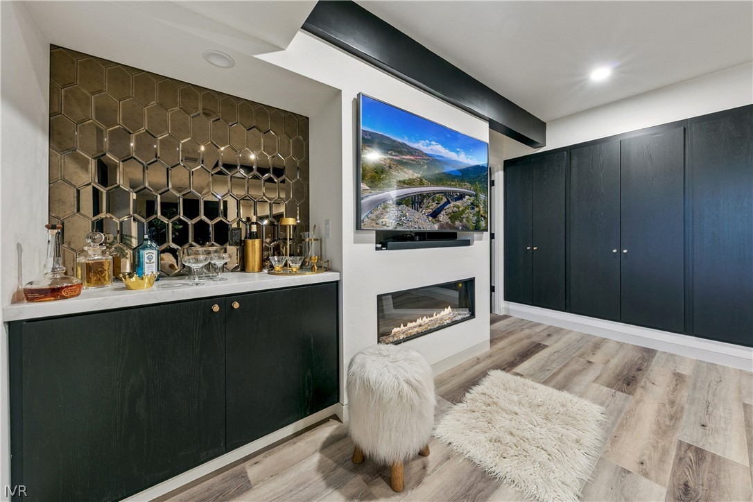 Modern bar with mirrored hexagon tiles, dark cabinets, a wall-mounted TV, and a linear fireplace.