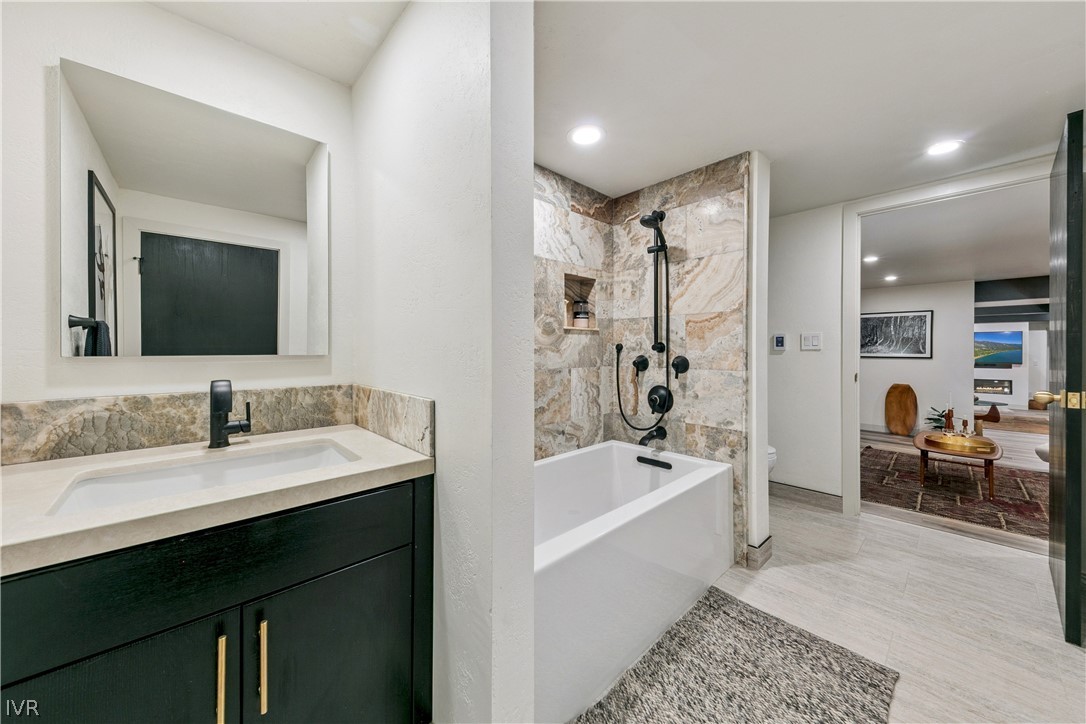 Bathroom with a stone-tile tub surround, matte black fixtures, and dark vanity.
