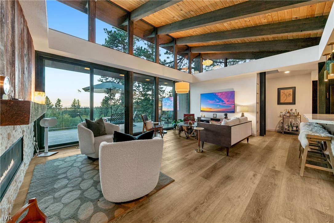 Living room with vaulted wood ceiling, stone fireplace, and floor-to-ceiling windows opening to a deck.