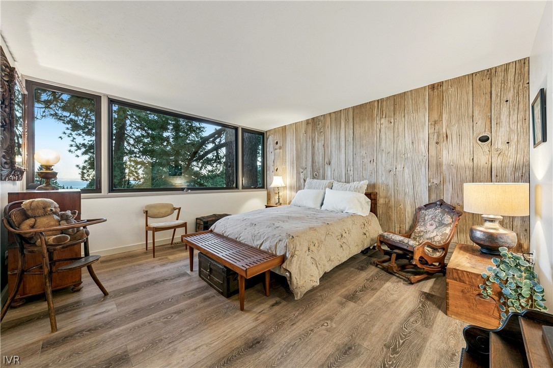 Bedroom with a rustic wood-plank wall, broad windows, and a glimpse of water.