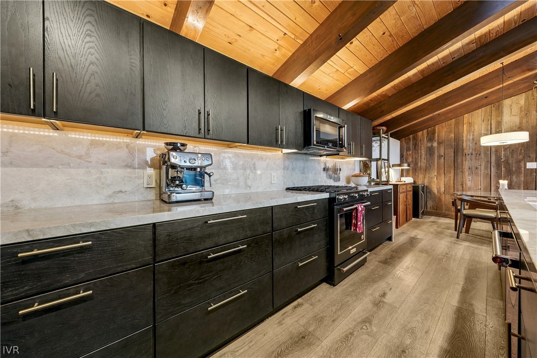 Kitchen with dark cabinetry, stone backsplash, vaulted wood ceiling, and adjacent dining area.