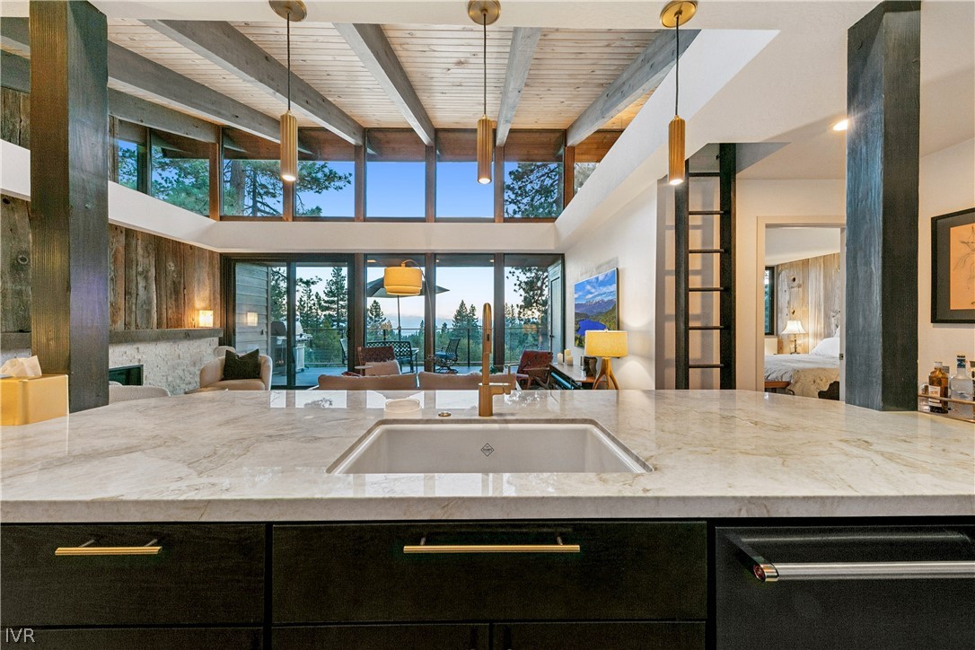 Open-plan kitchen with a marble island, exposed wood beams, and windows overlooking water and mountains.