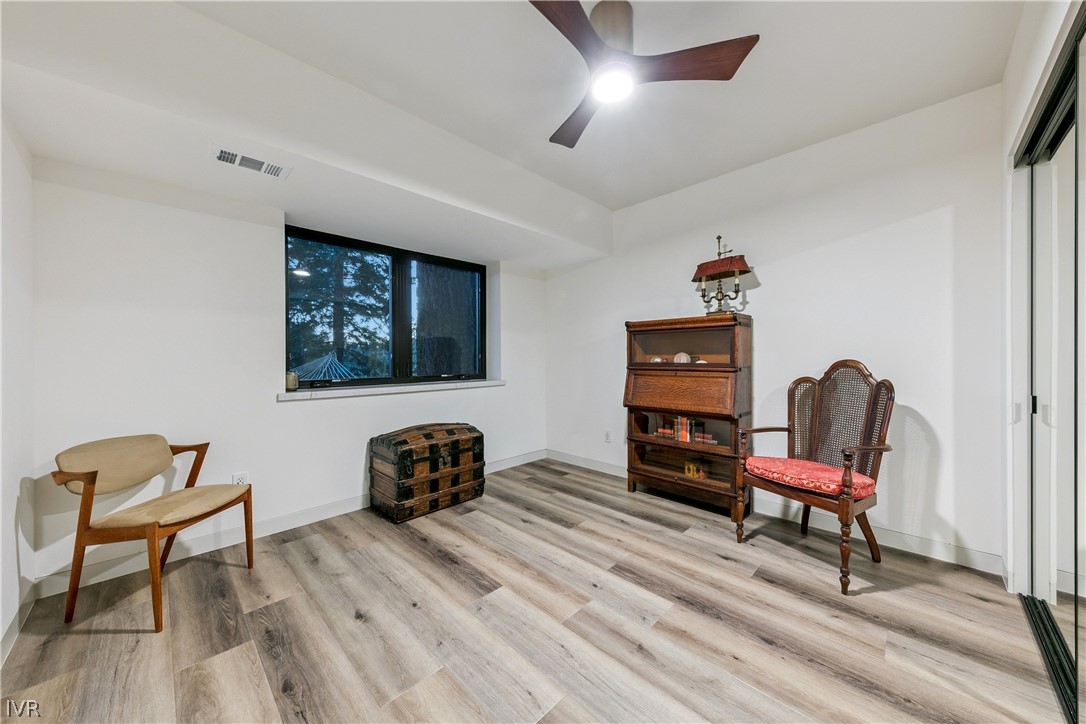 Furnished room with a tree-view window, wood-look floors, a bookcase, trunk, and two chairs.