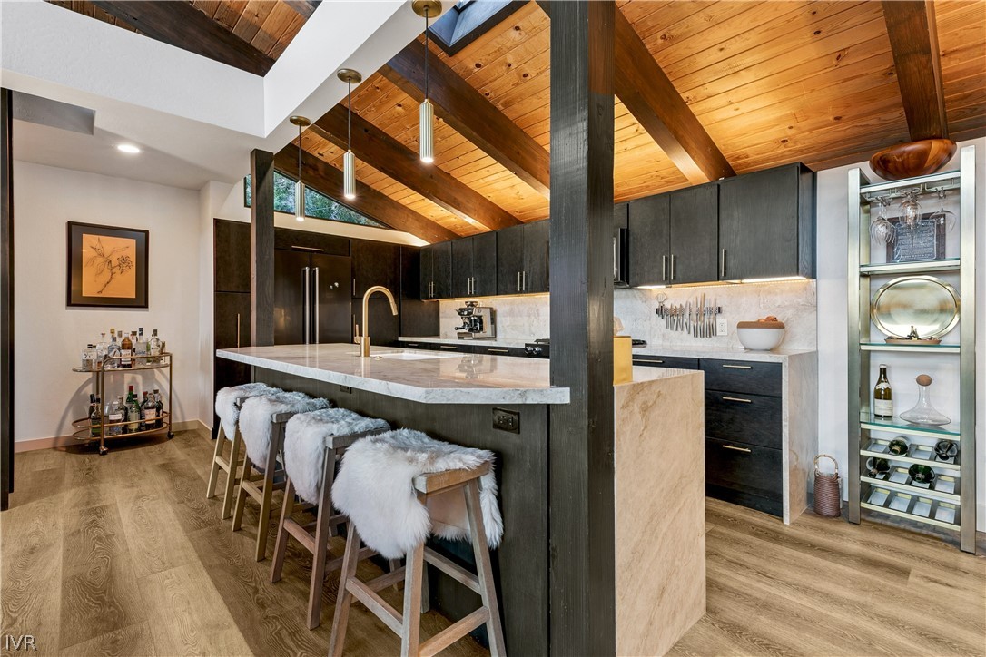 Kitchen with a marble island, dark cabinets, and vaulted wood ceiling with exposed beams.