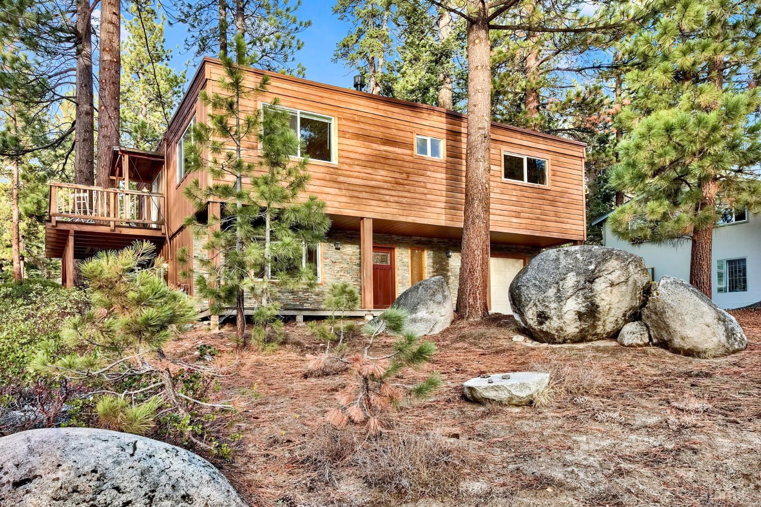 Wood-sided home among tall pines and granite boulders, with a raised side deck.