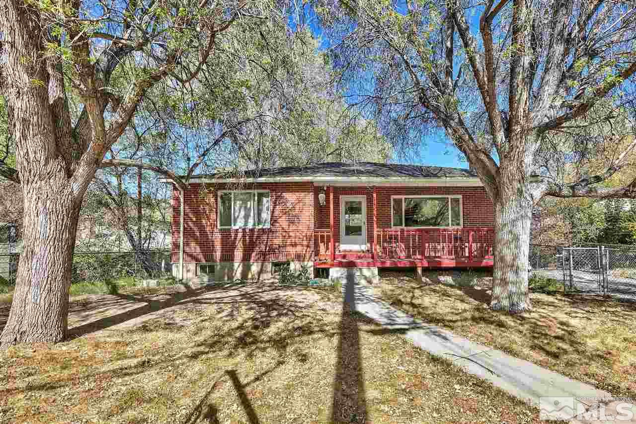 Red brick home with a covered porch, framed by mature trees and a fenced yard.