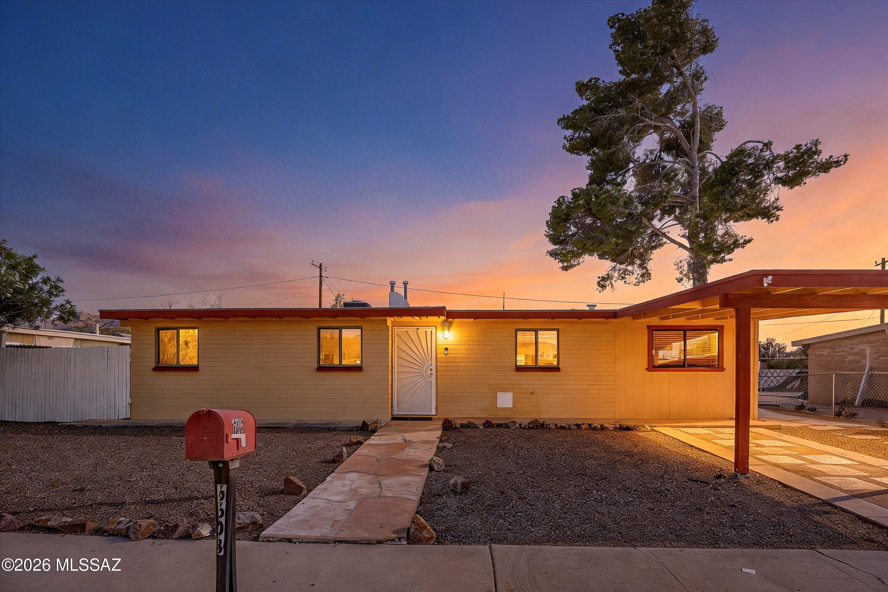 Single-story home with a covered carport and gravel yard at dusk.