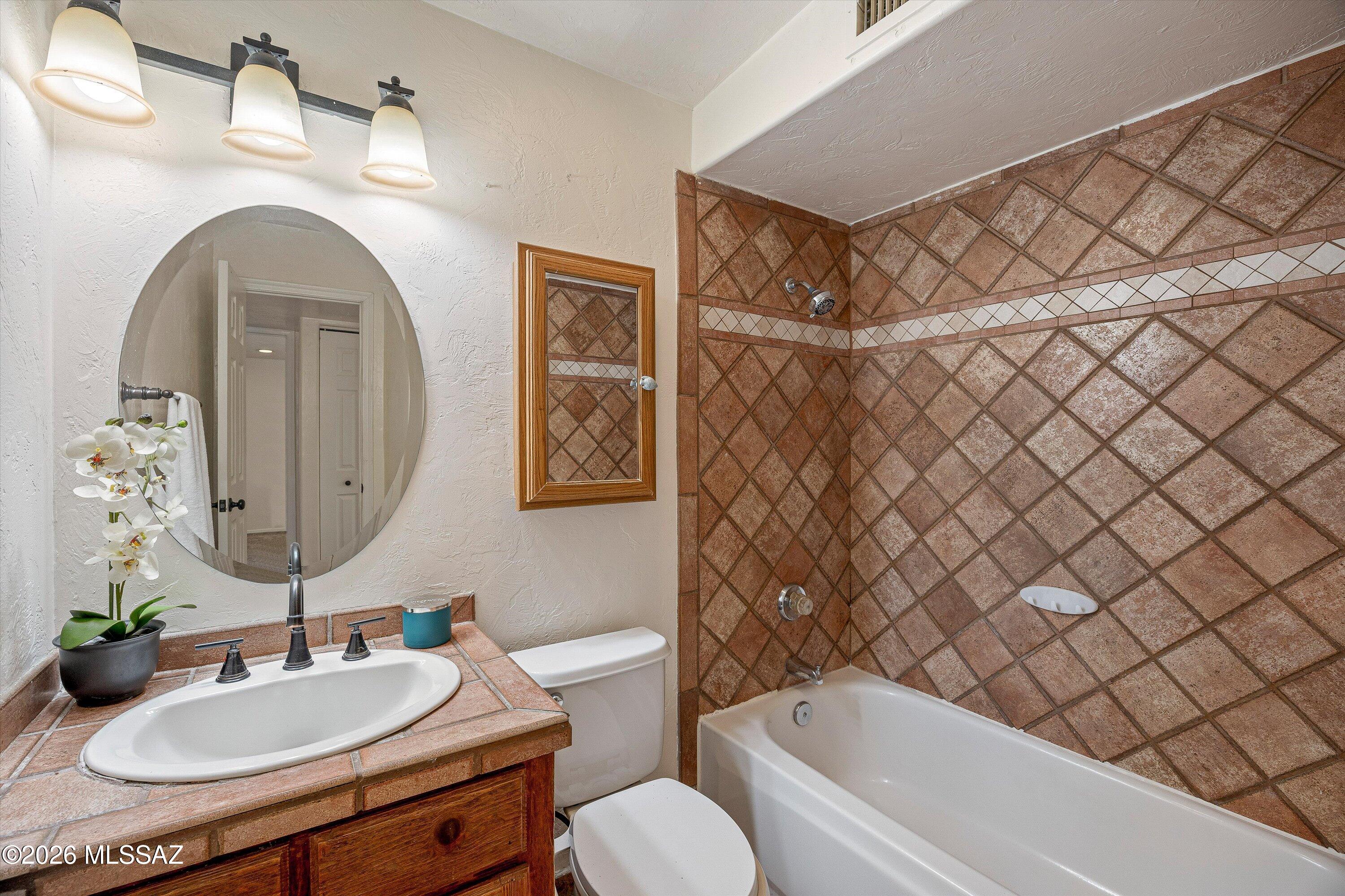 Bathroom with a tiled tub and shower, tiled vanity, oval mirror, and dark wood cabinetry.