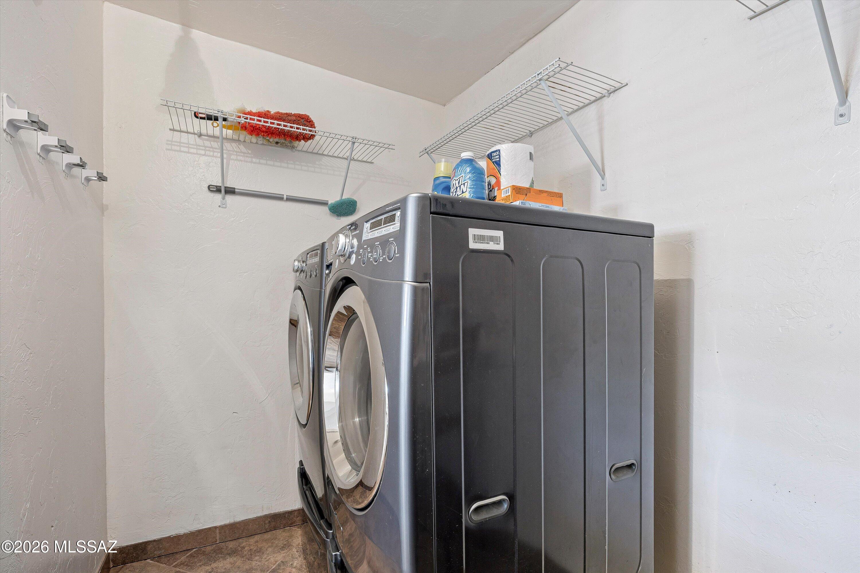 Laundry room with front-loading washer and dryer beneath wire storage shelves.