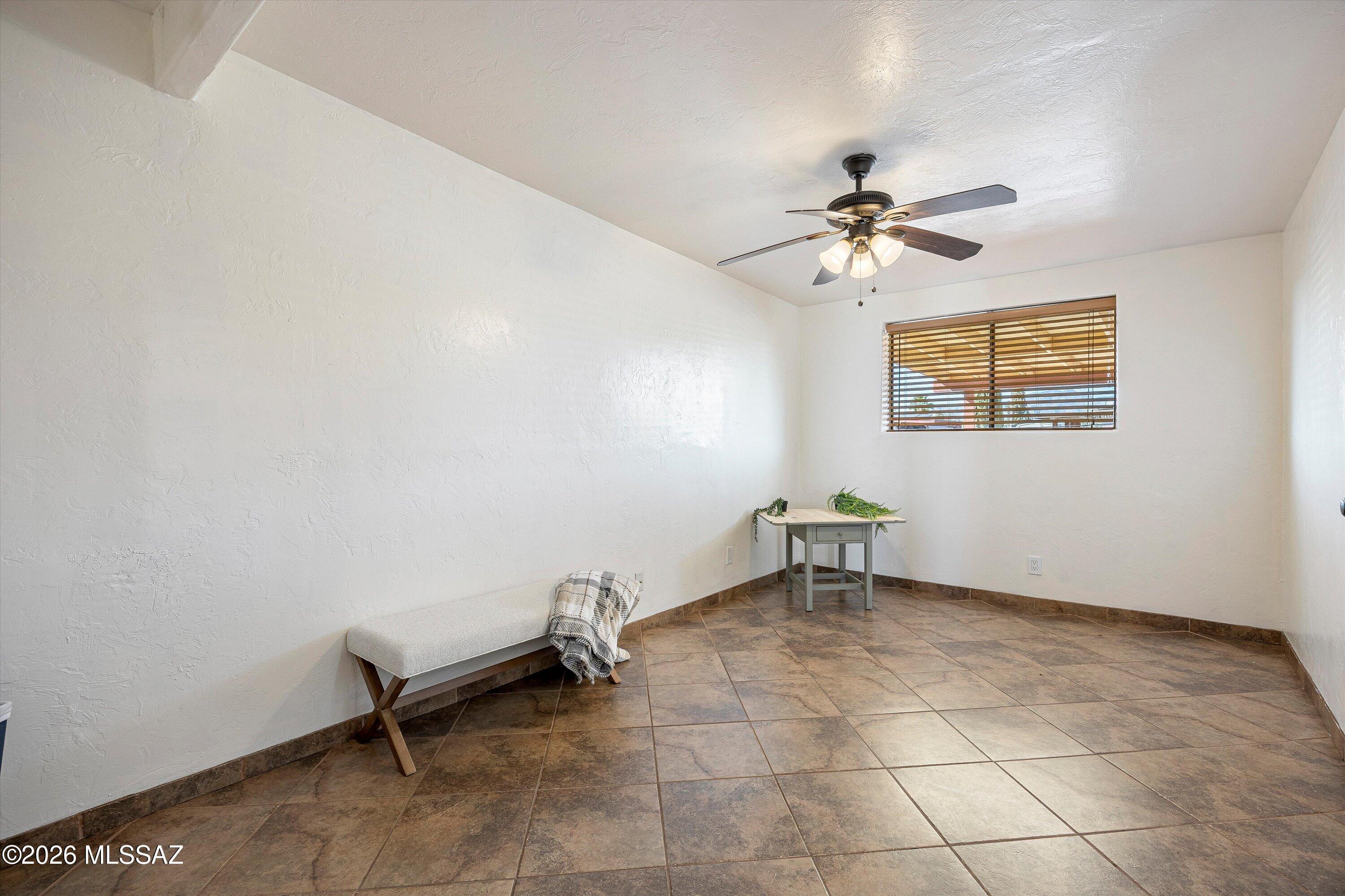 Sparse room with brown tile flooring, a ceiling fan, and a window with wooden blinds.
